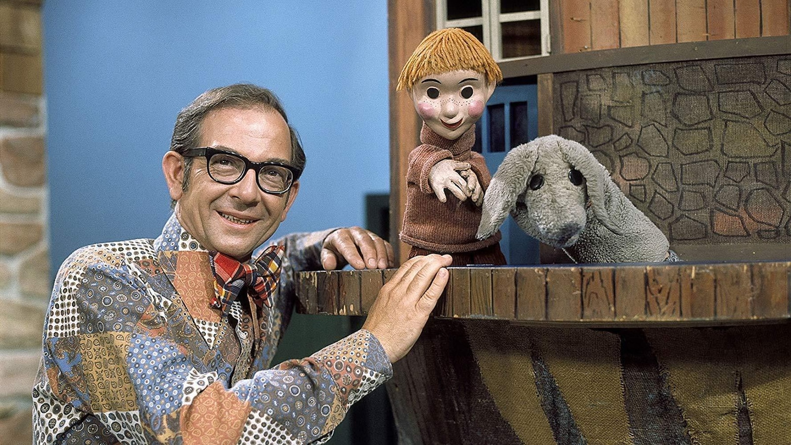 L'homme pose dans le décor de l'émission avec deux marionnettes.