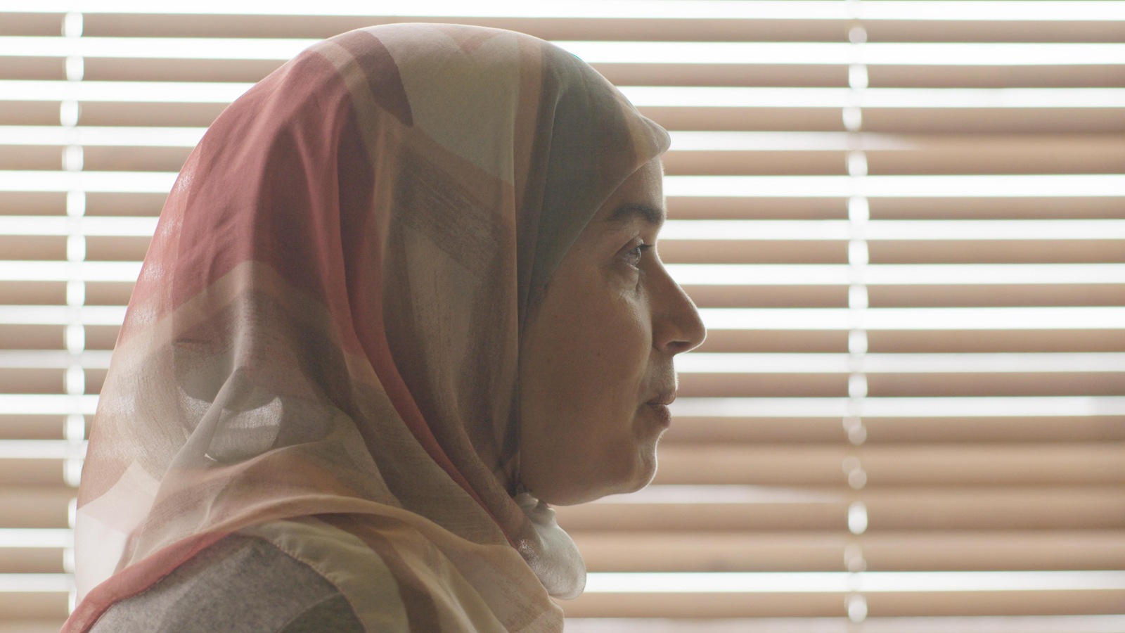 Une femme portant un hijab de profil devant des stores. Une femme portant un hijab de profil devant des stores.