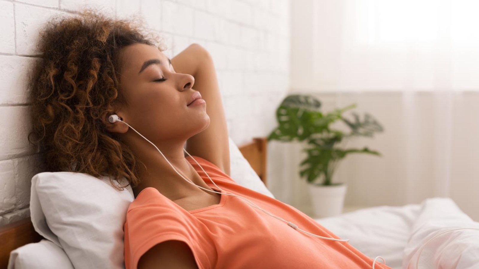 Une femme, couchée dans son lit, écoute de la musique avec des écouteurs sur la tête.