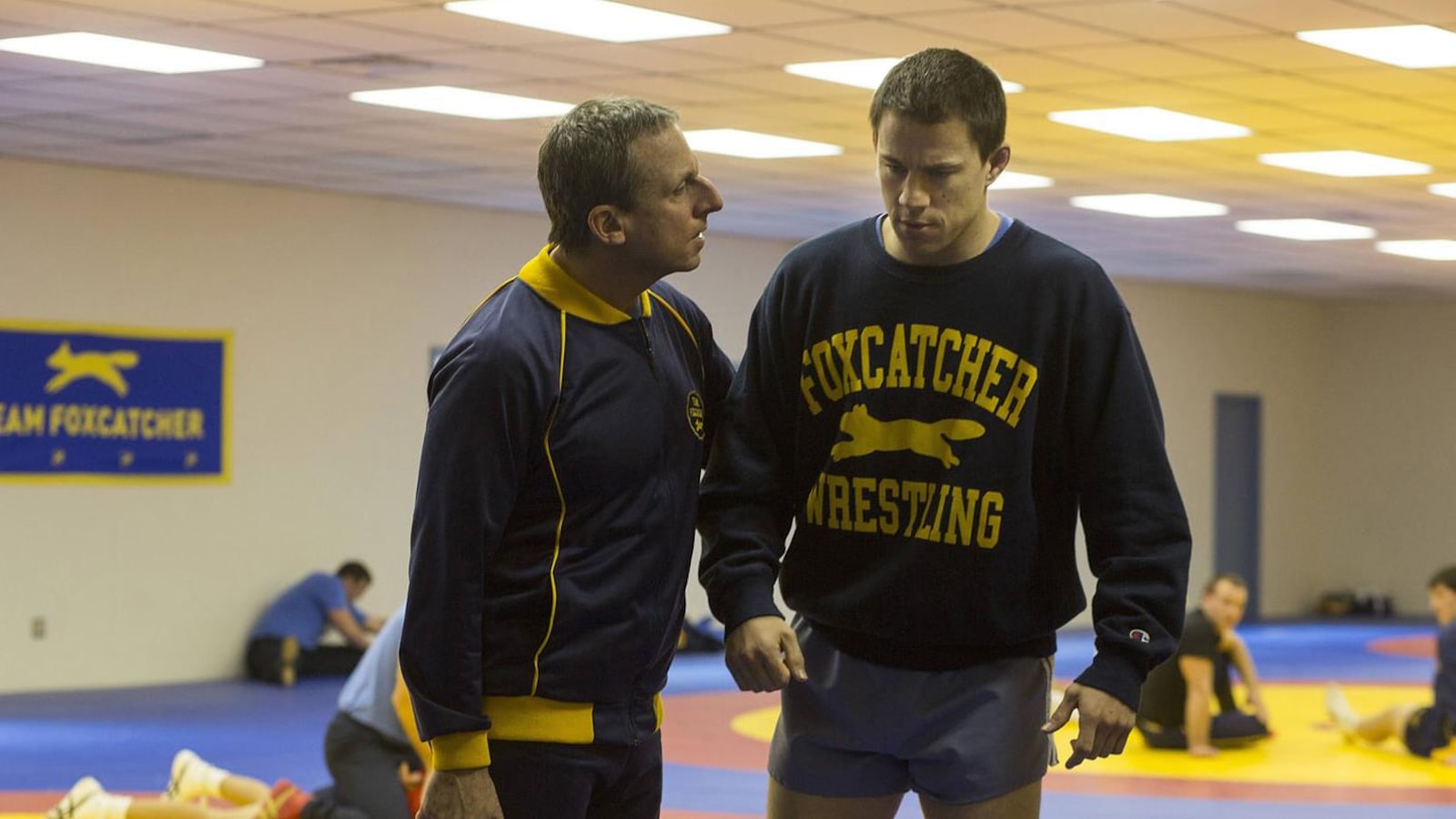 Un entraîneur (Steve Carrell) et un lutteur (Channing Tatum) dans un gymnase. Un entraîneur (Steve Carrell) et un lutteur (Channing Tatum) dans un gymnase.