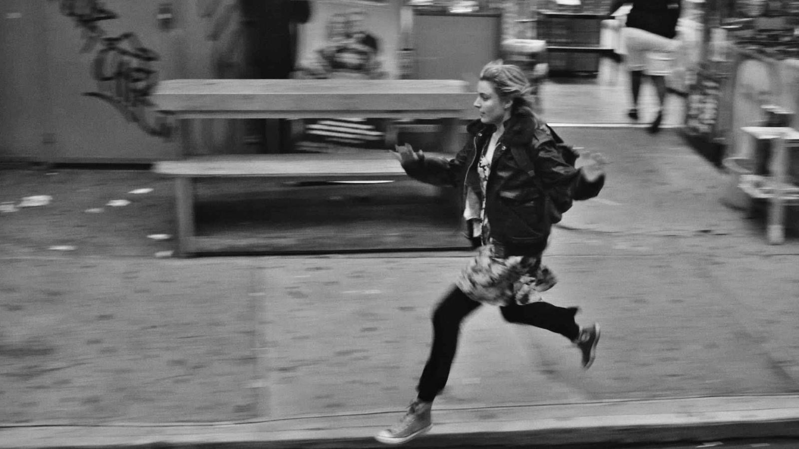 En noir et blanc, une jeune fille (Greta Gerwig) court dans la rue. En noir et blanc, une jeune fille (Greta Gerwig) court dans la rue.