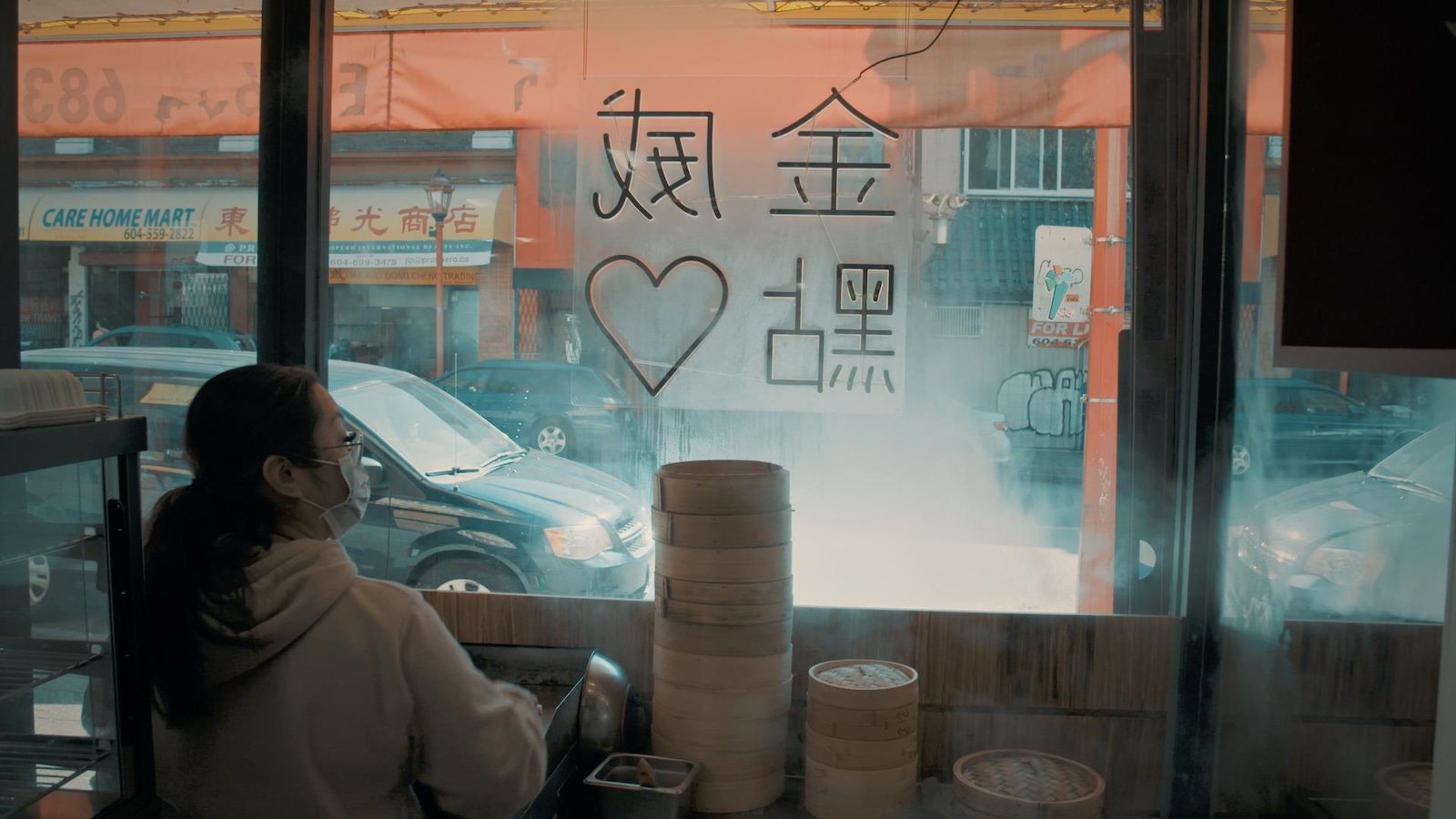 Un femme, dans un commerce d'un quartier chinois, regarde par la fenêtre