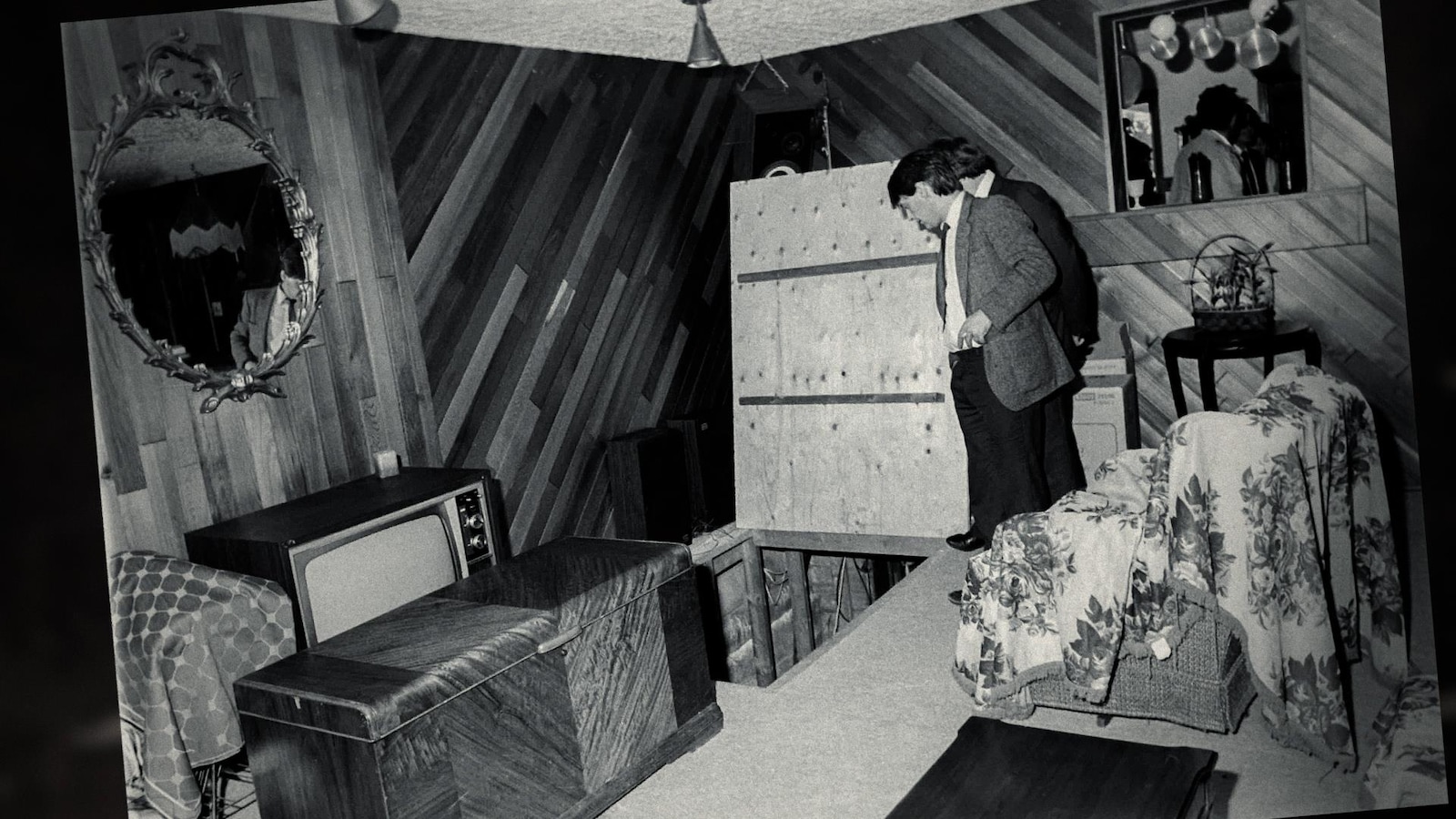 Photo en noir et blanc d'un enquêteur qui fait une fouille dans une chambre.
