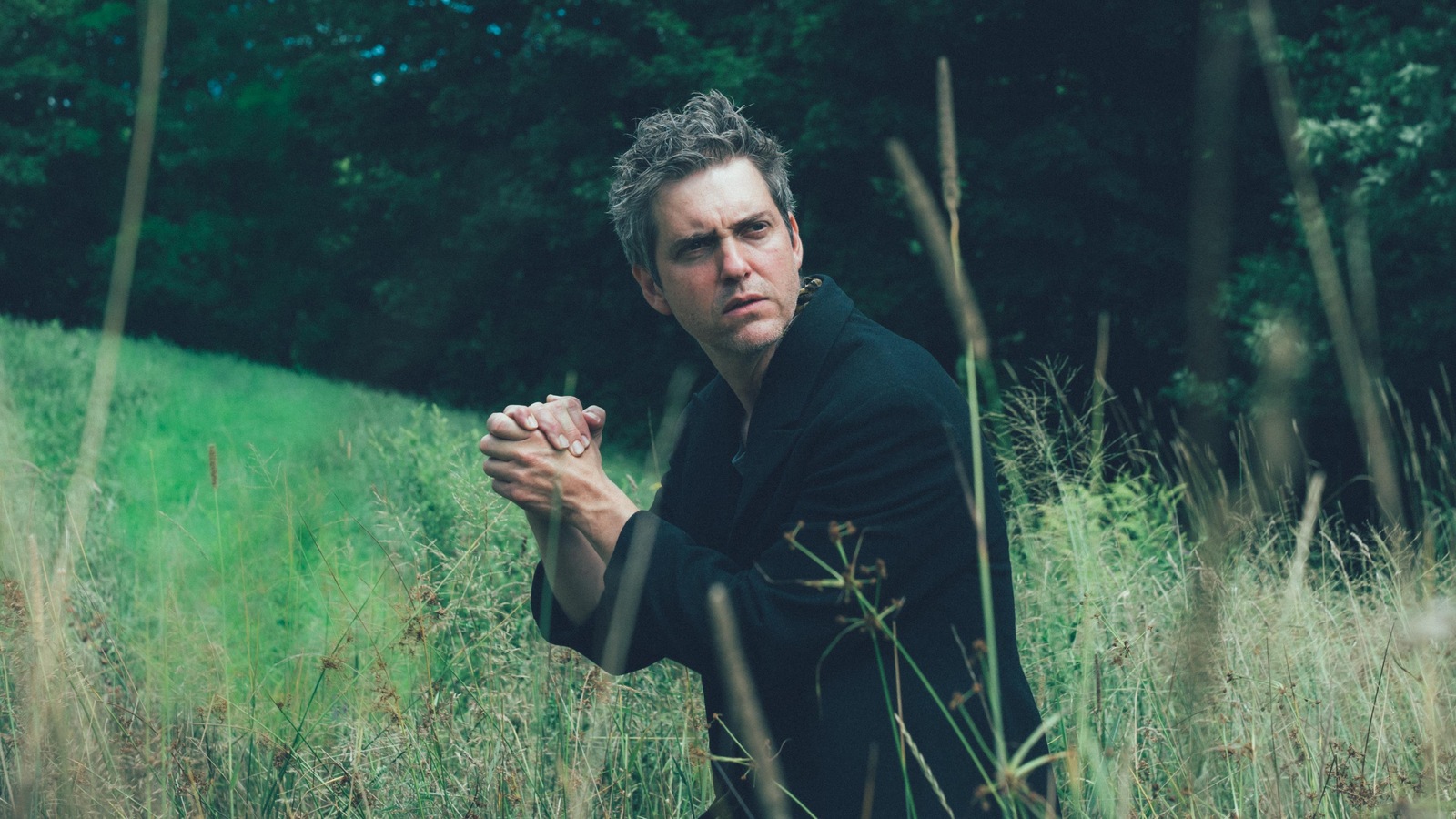 Un homme (Maxim Gaudette) les mains jointes, dans des herbes hautes. Un homme (Maxim Gaudette) les mains jointes, dans des herbes hautes.