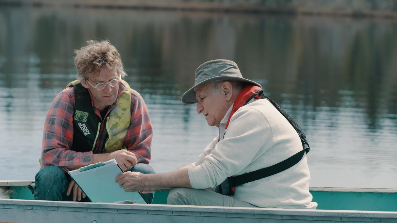 Les deux hommes sont assis dans une barque et regardent une feuille.