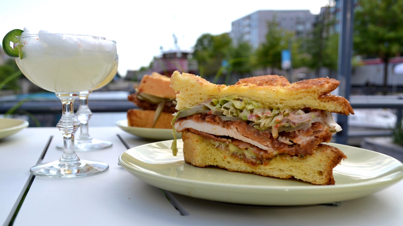 Un sandwich au poulet déposé sur une assiette accompagné d'un cocktail.