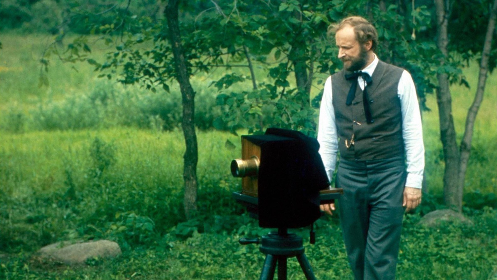 Un homme se tient derrière un appareil photo du début du siècle, en pleine nature. Un homme se tient derrière un appareil photo du début du siècle, en pleine nature.