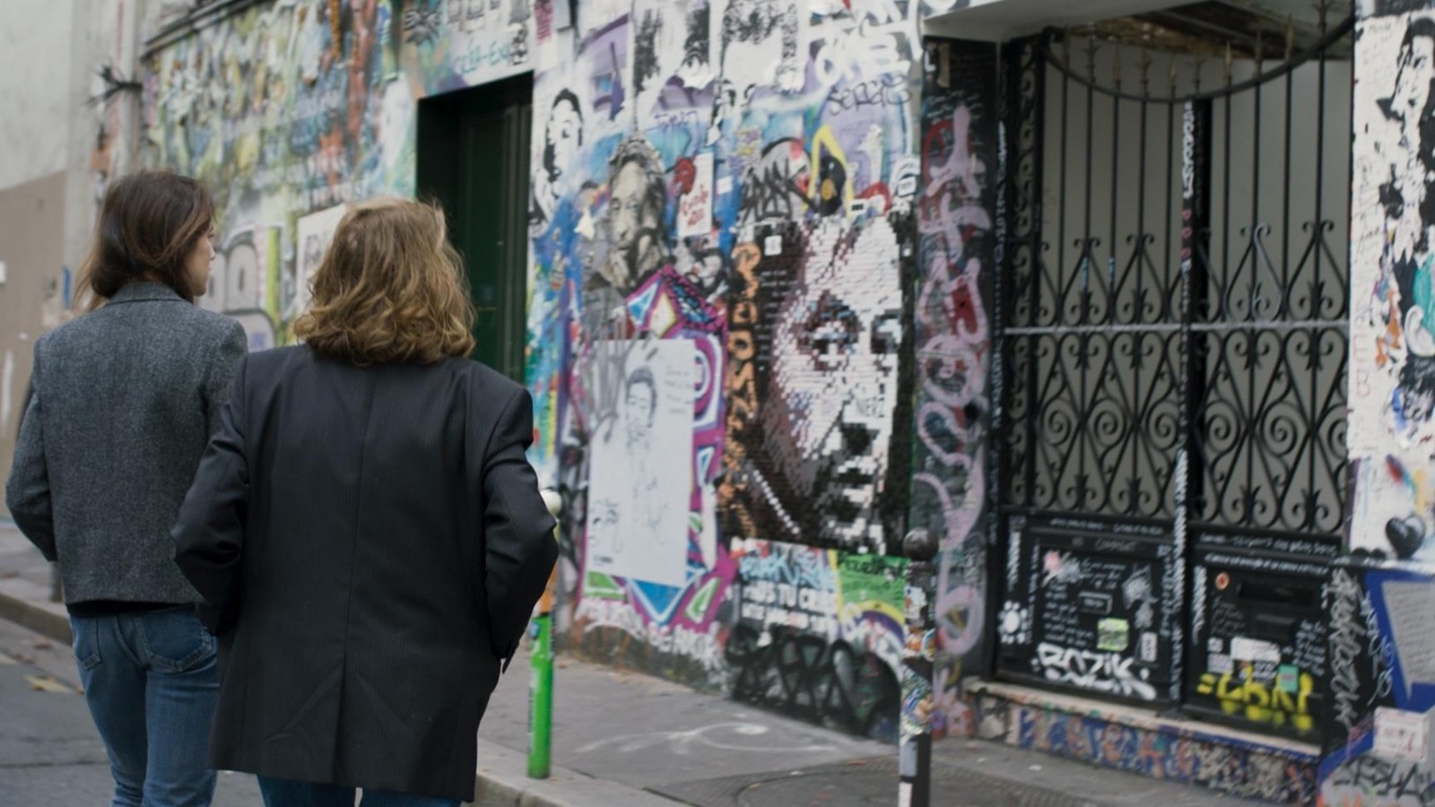 Deux femmes (Charlotte Gainsbourg et Jane Birkin) de dos, devant une façade bariolée où on voit le visage de Serge Gainsbourg dessiné. Deux femmes (Charlotte Gainsbourg et Jane Birkin) de dos, devant une façade bariolée où on voit le visage de Serge Gainsbourg dessiné.