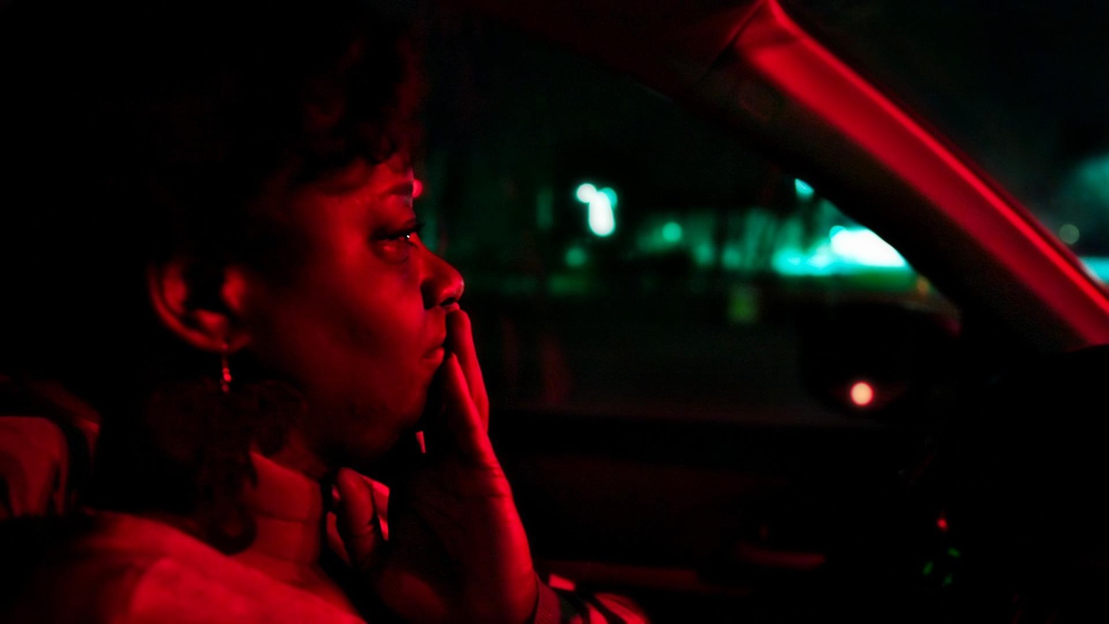 A woman in her car, in profile, under red lighting.