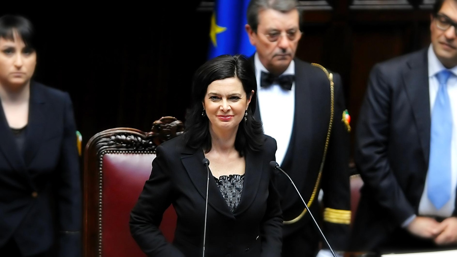 In a parliament, a woman standing in front of two microphones.