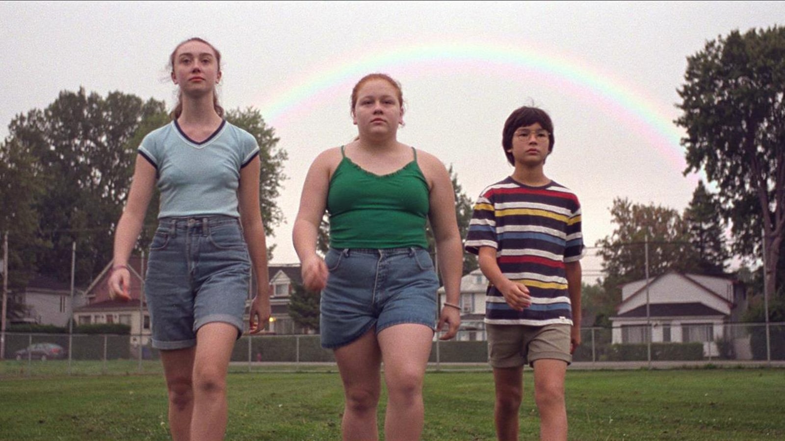 Trois adolescents marchent dans l'herbe, un arc-en-ciel derrière eux. Trois adolescents marchent dans l'herbe, un arc-en-ciel derrière eux.