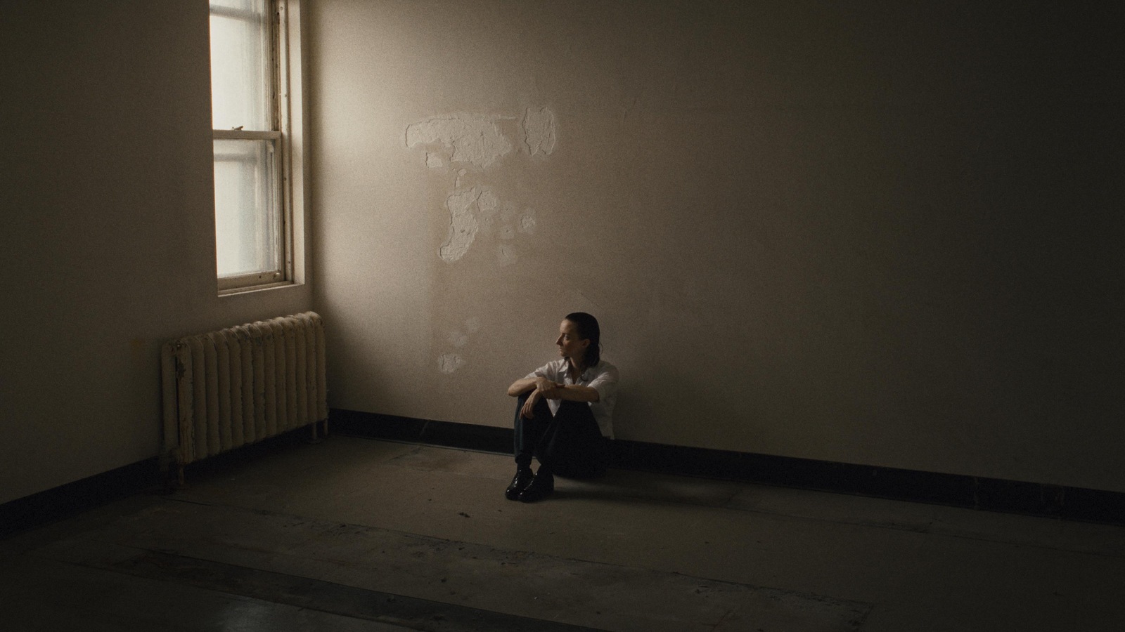 Une femme (Larissa Corriveau) assise par terre dans une pièce vide.