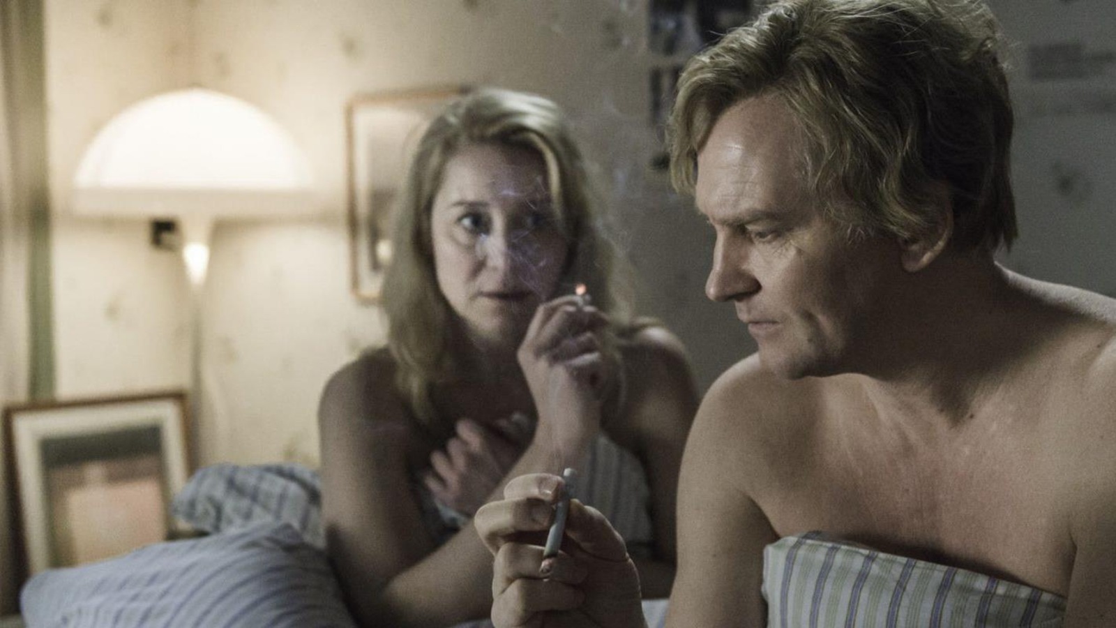 Un homme et une femme, l'air soucieux, fument une cigarette dans leur lit. Un homme et une femme, l'air soucieux, fument une cigarette dans leur lit.