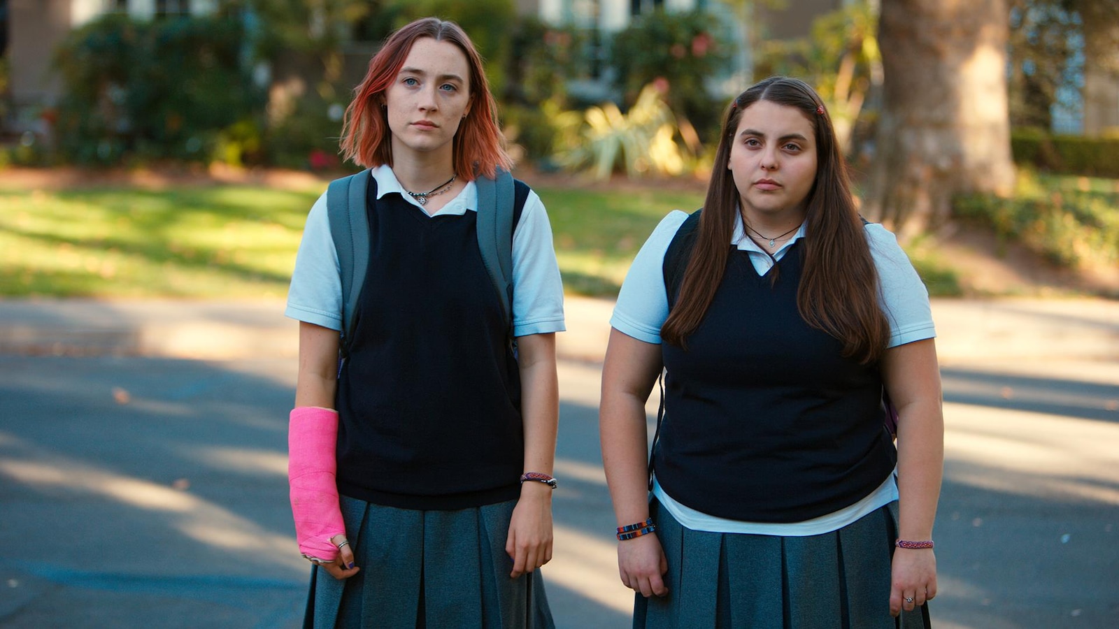 Two young women in school uniforms are walking down the street.