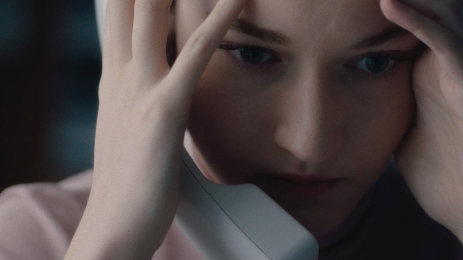 Une jeune femme, la tête entre les mains et un combiné de téléphone sur l'oreille, en très gros plan.