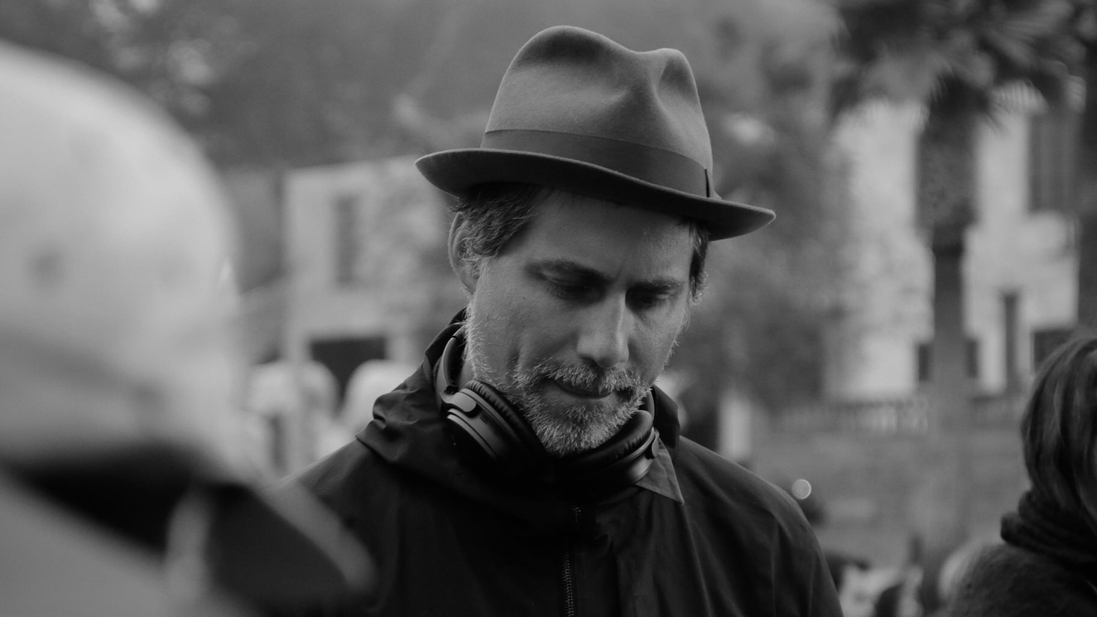 En noir et blanc, un homme portant un chapeau et des écouteurs autour du cou.