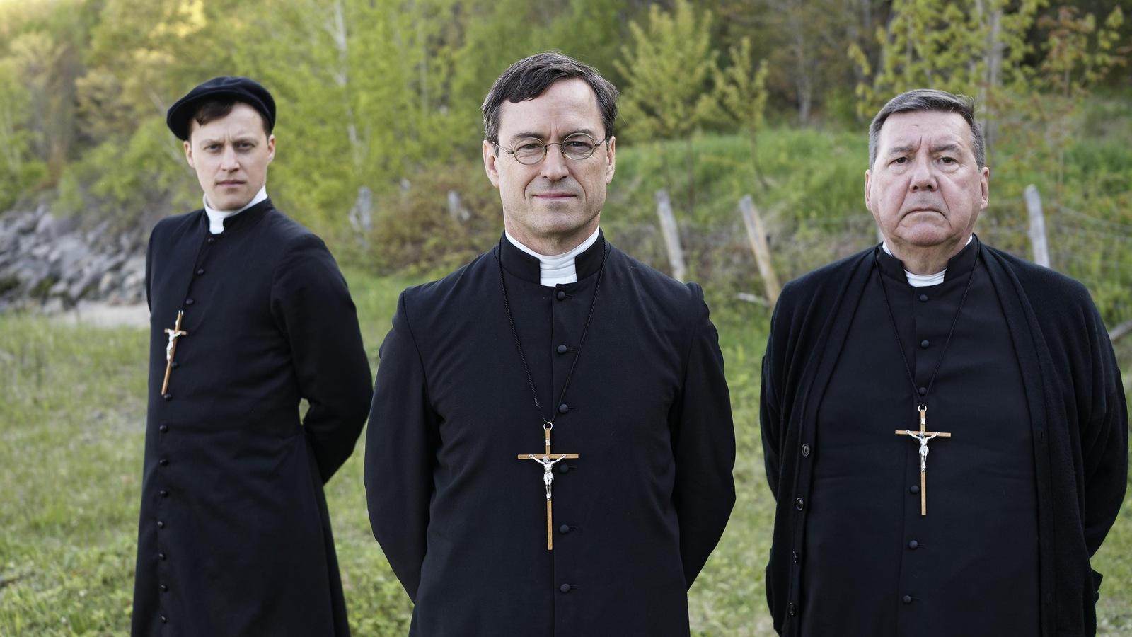Dans un champ, trois hommes habillés en prêtres (dont Sébastien Ricard et Rémy Girard) regardent la caméra. Dans un champ, trois hommes habillés en prêtres (dont Sébastien Ricard et Rémy Girard) regardent la caméra.