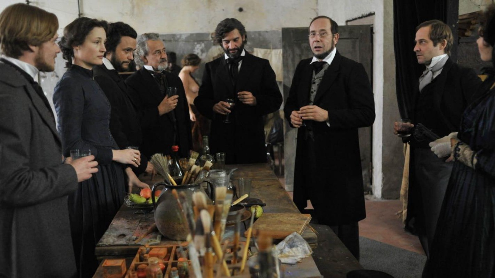 Un groupe d'hommes et une femme en tenue d'époque debout autour d'une table. Un groupe d'hommes et une femme en tenue d'époque debout autour d'une table.