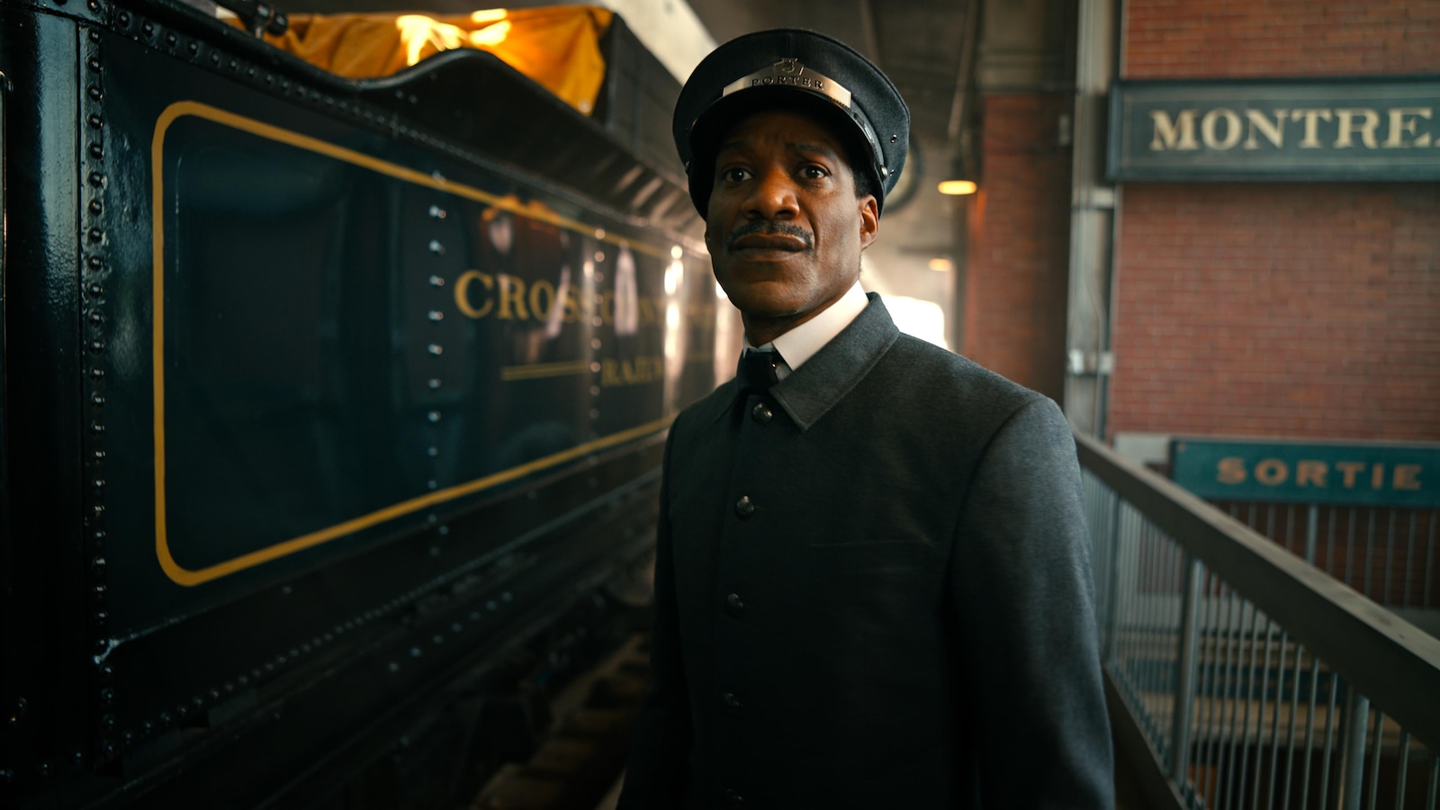 Un porteur en uniforme se tient sur un quai à côté d'un train.