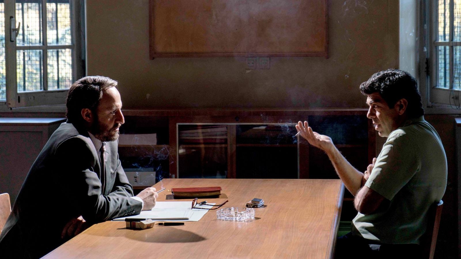 Deux hommes se parlent, assis face à face autour d'une table. Deux hommes se parlent, assis face à face autour d'une table.