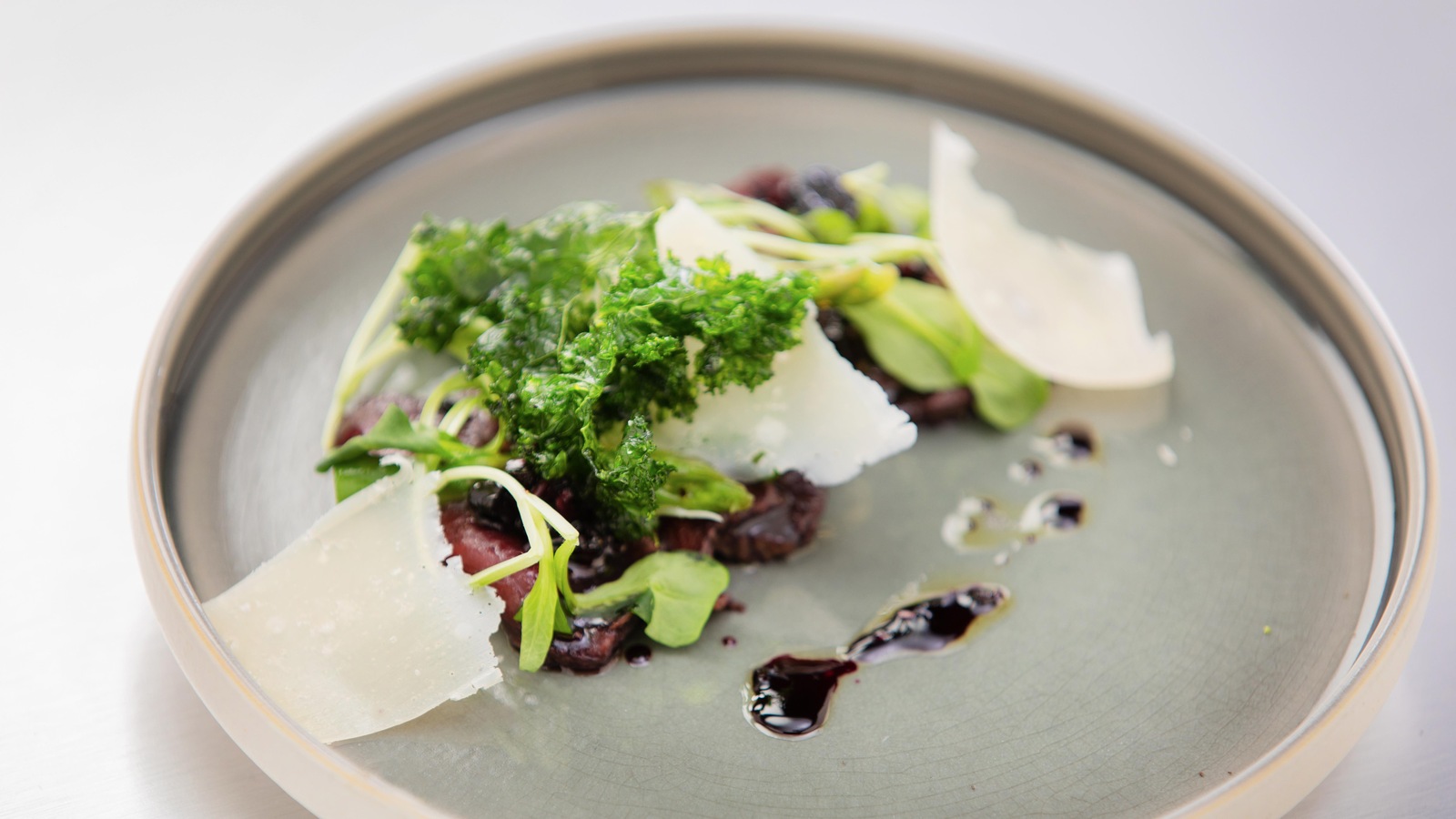 Assiette rondes avec des gouttes de sauce, des copeaux de parmesan. Les lamelles sont recouvertes de verdure. Assiette rondes avec des gouttes de sauce, des copeaux de parmesan. Les lamelles sont recouvertes de verdure.