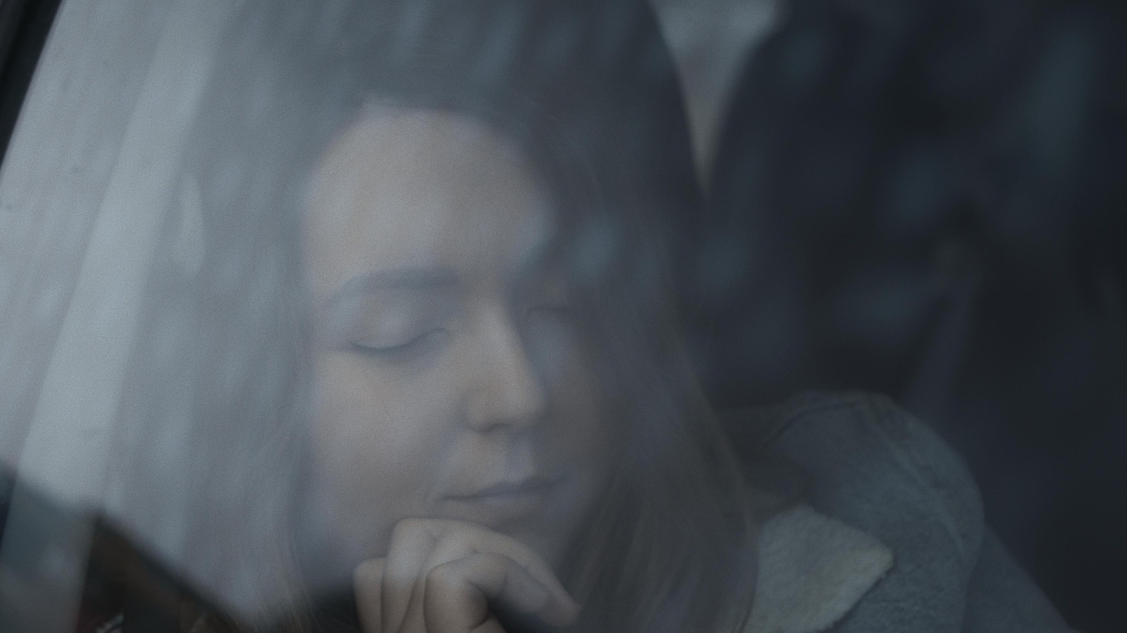 Une jeune femme, les yeux fermés, filmée à travers une vitre de voiture. Une jeune femme, les yeux fermés, filmée à travers une vitre de voiture.