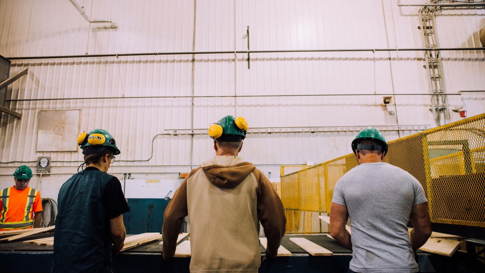 Trois hommes de dos devant la chaîne de montage d'une scierie. Trois hommes de dos devant la chaîne de montage d'une scierie.