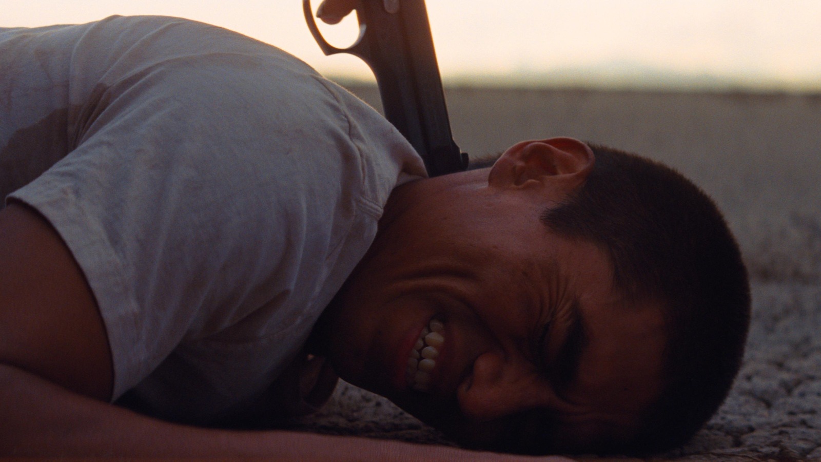 Un jeune homme couché sur le sol, sur le ventre, grimace tandis que le canon d'un revolver pointe sa nuque. Un jeune homme couché sur le sol, sur le ventre, grimace tandis que le canon d'un revolver pointe sa nuque.