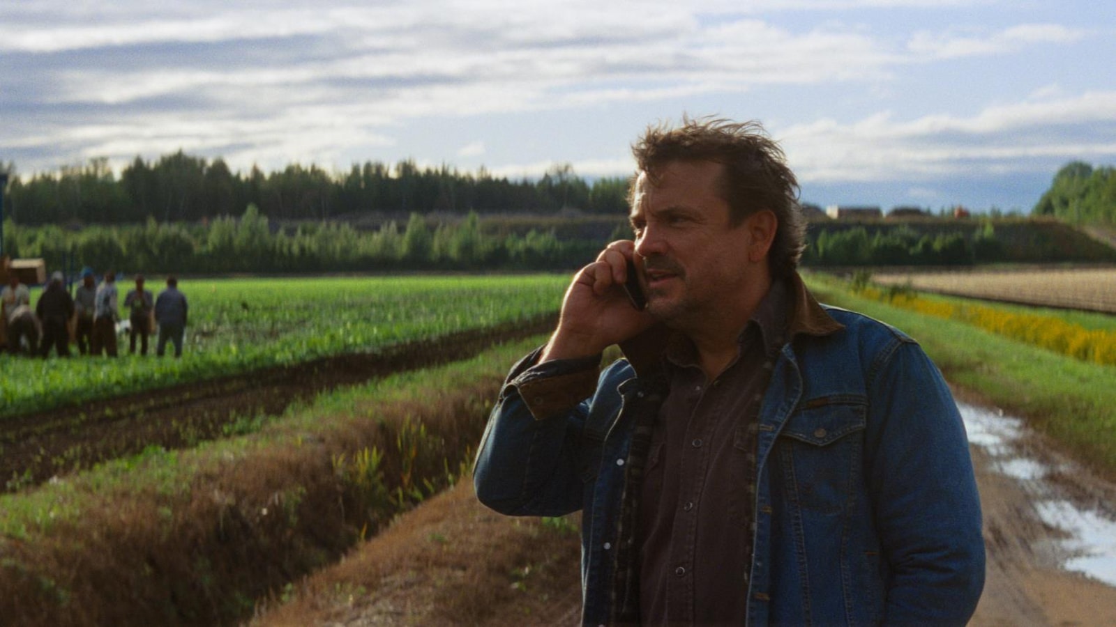 Un homme (Claude Legault) téléphone devant un champ où des travailleurs saisonniers sont regroupés. Un homme (Claude Legault) téléphone devant un champ où des travailleurs saisonniers sont regroupés.