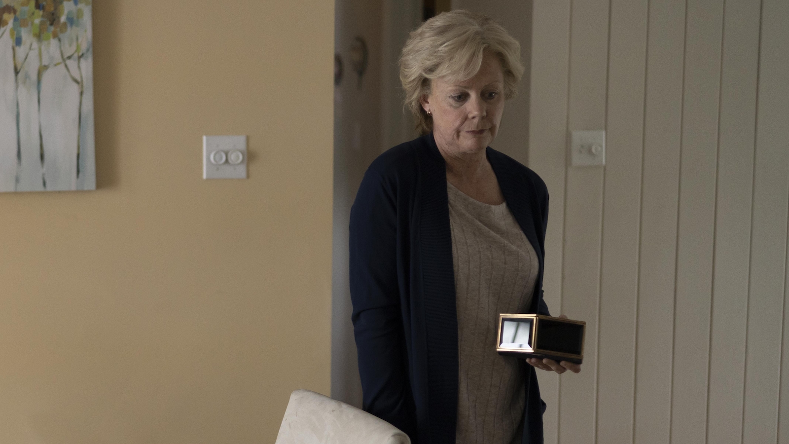 Lorraine (Anie Pascale) tient une boîte en métal dans une main, sa canne dans l'autre main.