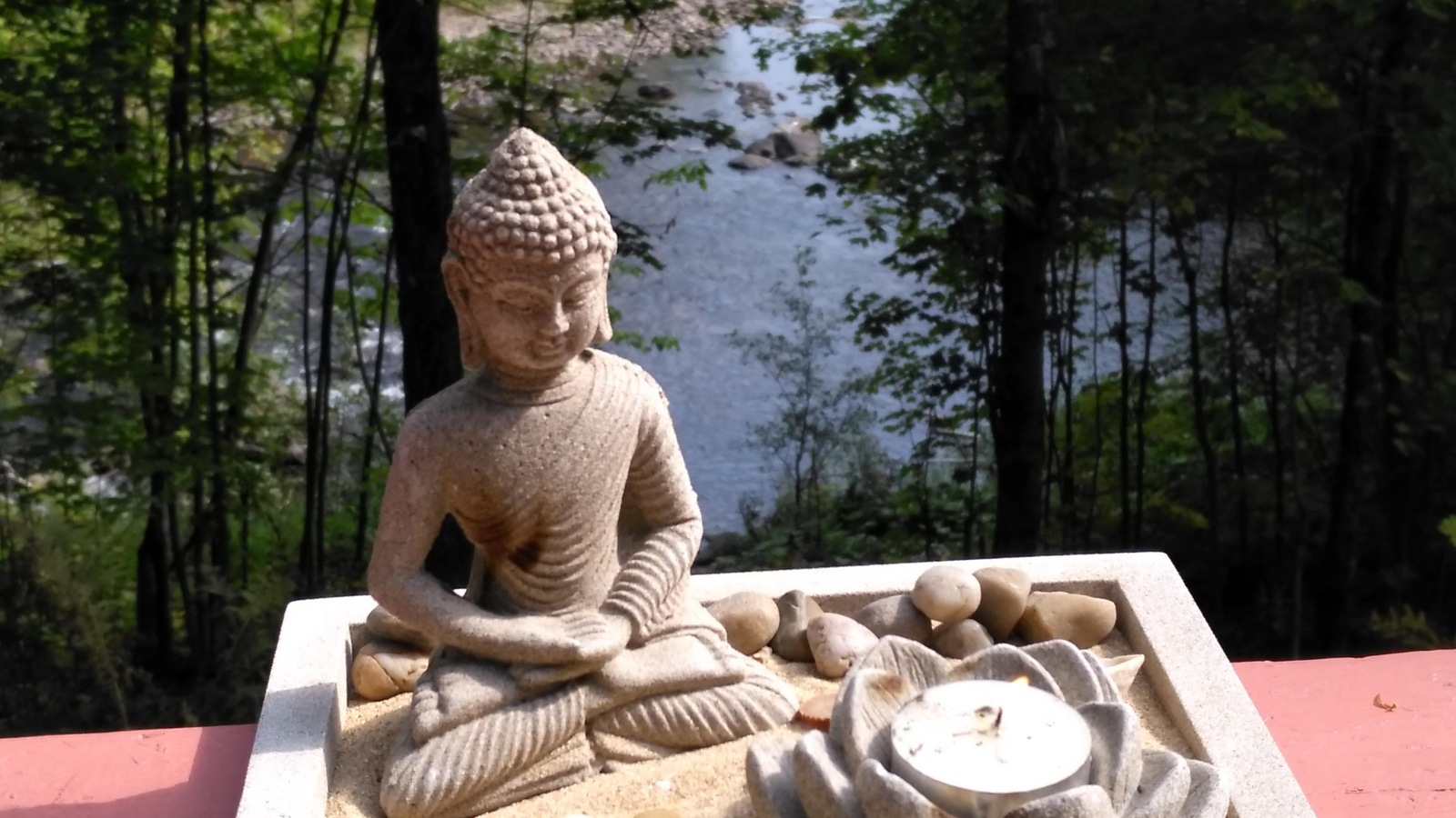 Une statuette dans un bac de sable qui contient des pierres et une chandelle dans une fleur de lotus est installé sur un balcon avec vue sur la rivière. Une statuette dans un bac de sable qui contient des pierres et une chandelle dans une fleur de lotus est installé sur un balcon avec vue sur la rivière.