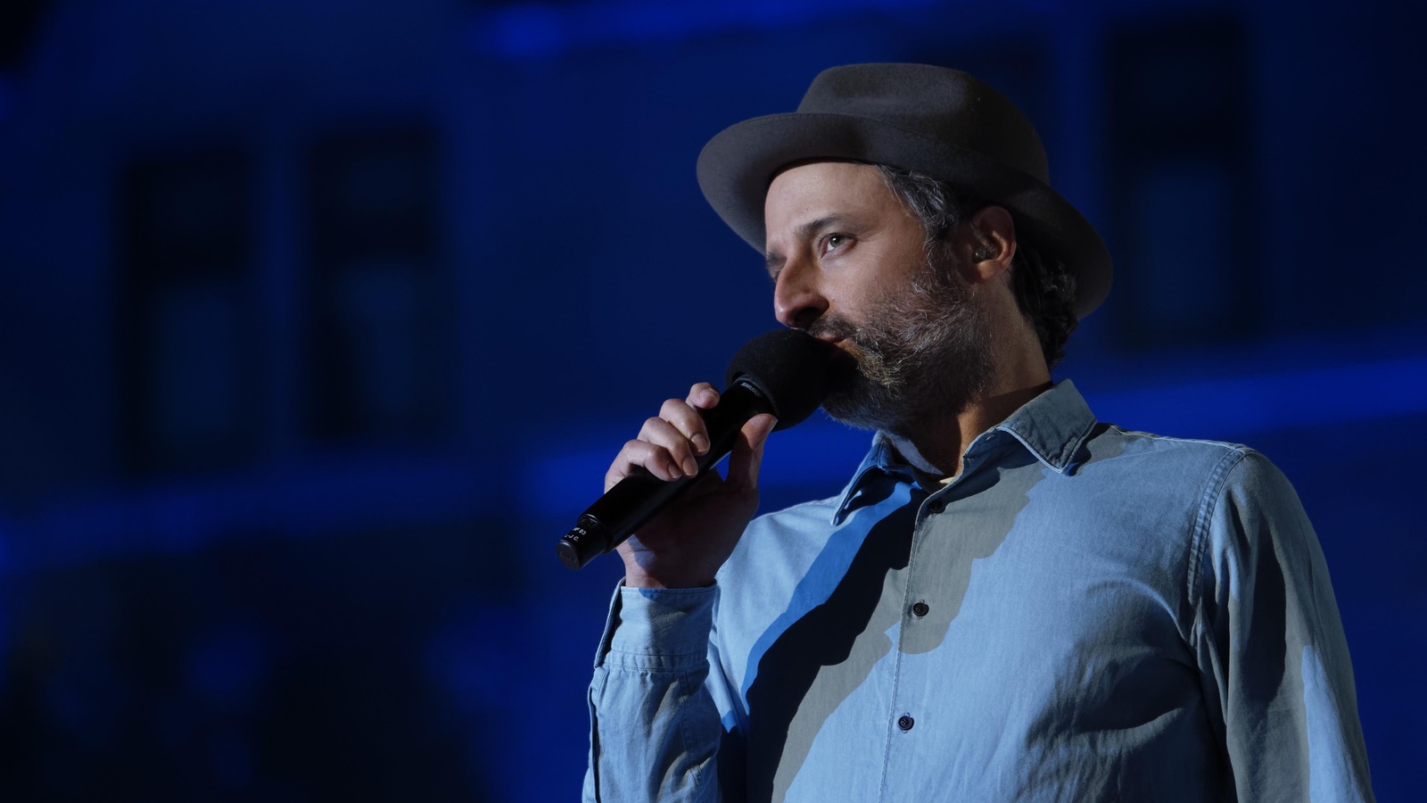 L'homme est sur une scène, il tient un micro et chante. L'homme est sur une scène, il tient un micro et chante.