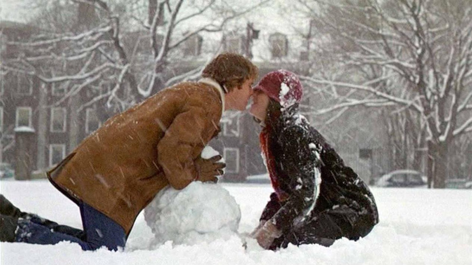 Un couple s'embrasse, sous la neige, au-dessus d'un bonhomme de neige qu'ils construisent. Un couple s'embrasse, sous la neige, au-dessus d'un bonhomme de neige qu'ils construisent.