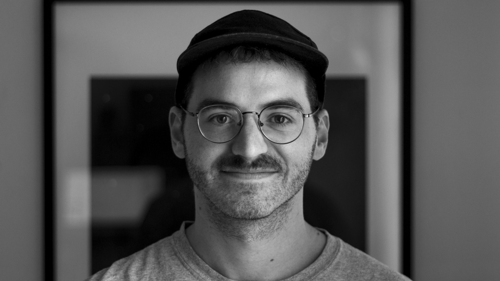 Un homme portant une casquette et des lunettes regarde droit devant lui, en noir et blanc. Un homme portant une casquette et des lunettes regarde droit devant lui, en noir et blanc.