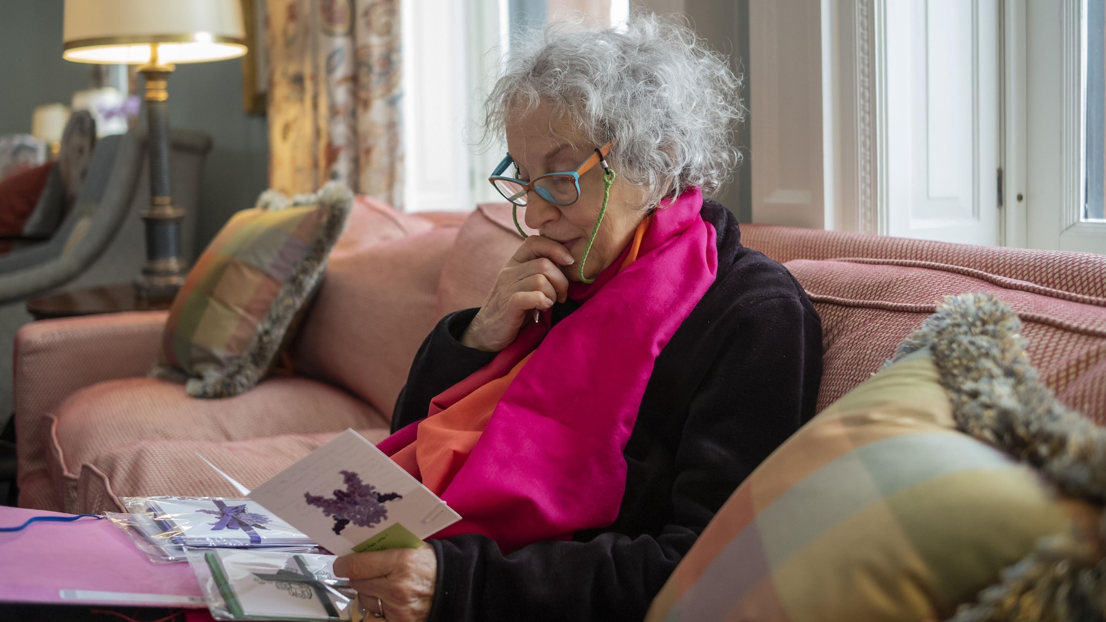 Margaret Atwood est assise sur un canapé rose. Elle lit une carte.
