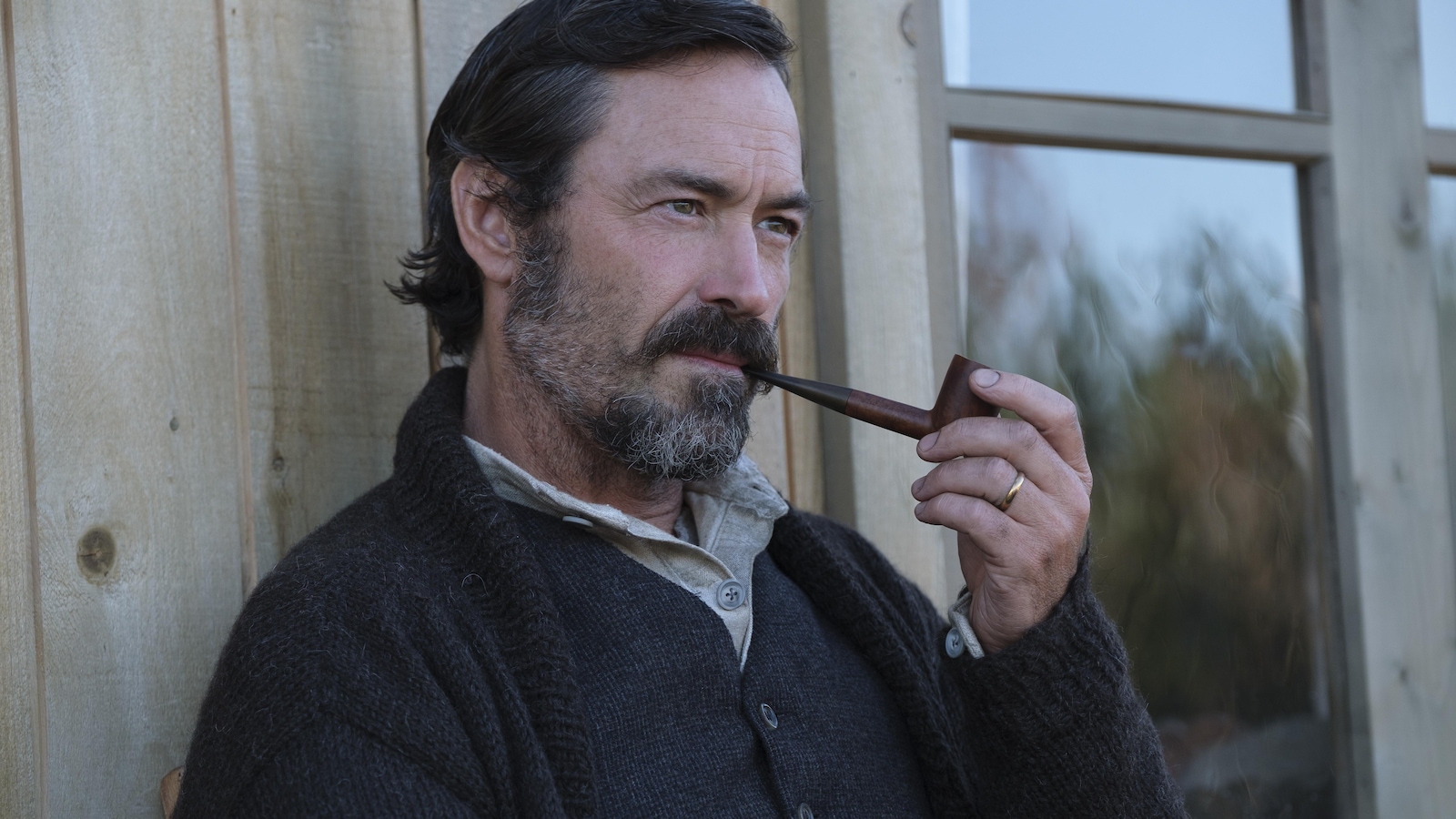 Un homme (Sébastien Ricard), l'air pensif, fume la pipe, devant une maison. Un homme (Sébastien Ricard), l'air pensif, fume la pipe, devant une maison.
