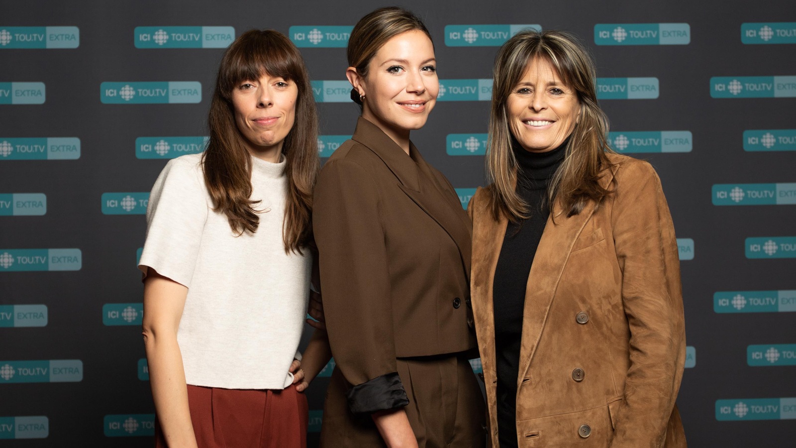 Les trois femmes sourient. Elle posent devant un panneau affichant le logo ICI Tou.tv Extra.