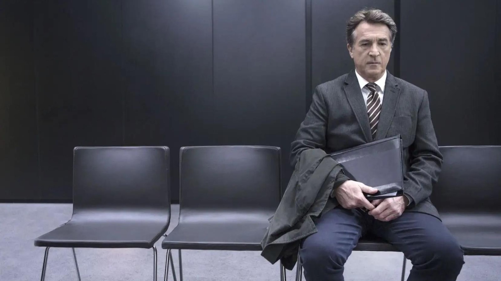 Un homme (François Cluzet) assis seul dans une salle d'attente.