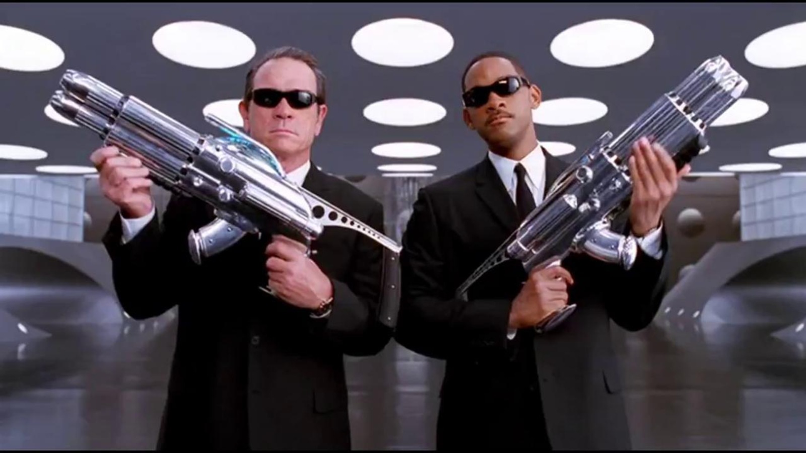 Deux hommes en costumes et lunettes noires tiennent d'énormes armes dans leurs bras Deux hommes en costumes et lunettes noires tiennent d'énormes armes dans leurs bras