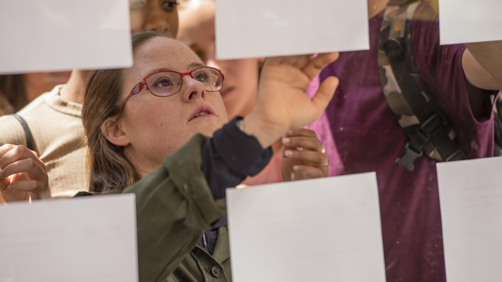 Une jeune fille cherche son nom et ses résultats sur des feuilles de papier accrochées sur une vitre. Une jeune fille cherche son nom et ses résultats sur des feuilles de papier accrochées sur une vitre.