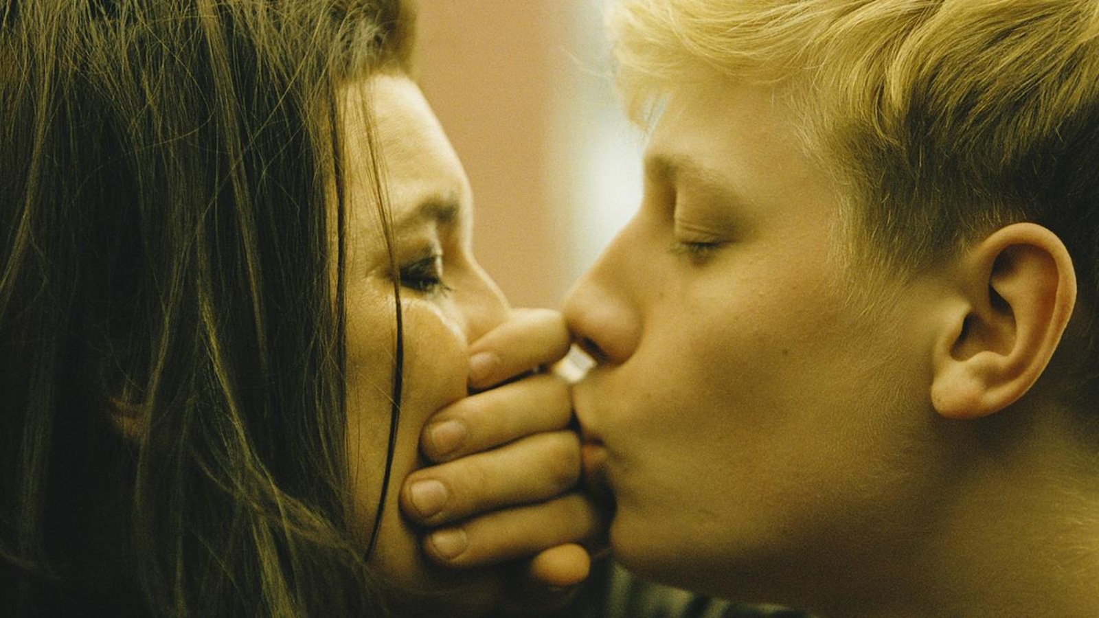 Un jeune homme embrasse une femme, la main entre leurs deux bouches Un jeune homme embrasse une femme, la main entre leurs deux bouches