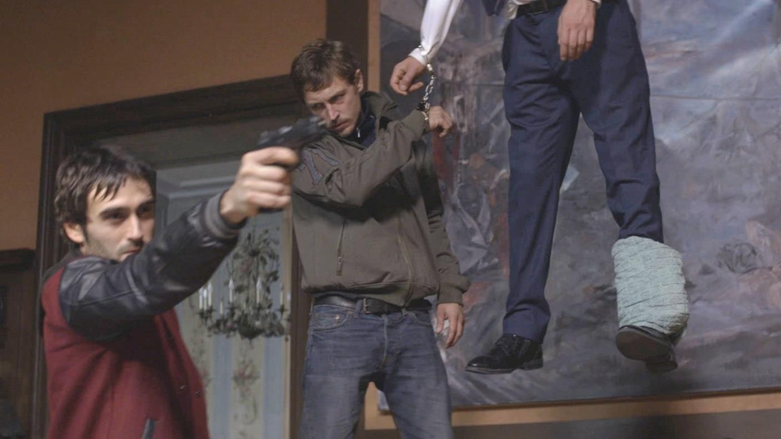 Un jeune homme tient un pistolet, un autre derrière lui est menotté à un pendu Un jeune homme tient un pistolet, un autre derrière lui est menotté à un pendu