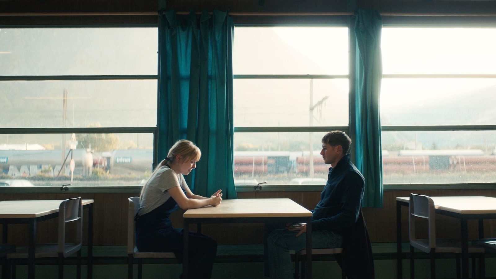 Une jeune fille et un homme (Bastien Bouillon) assis face à face, autour d'une table.