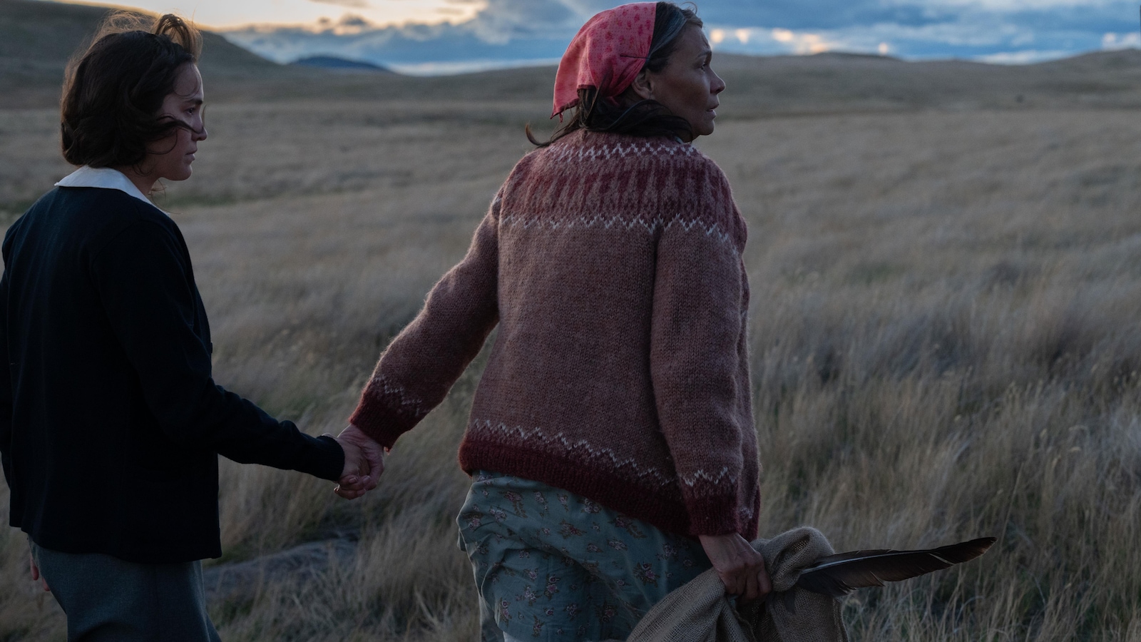 Une femme marche dans des champs en tenant une jeune fille par la main.