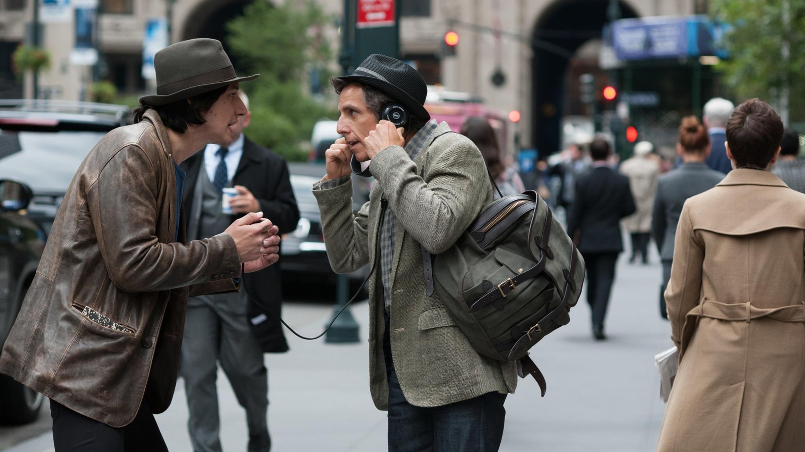 Dans la rue, un homme portant un chapeau (Adam Driver) fait écouter avec des écouteurs quelque chose à un autre homme portant aussi un chapeau (Ben Stiller). Dans la rue, un homme portant un chapeau (Adam Driver) fait écouter avec des écouteurs quelque chose à un autre homme portant aussi un chapeau (Ben Stiller).