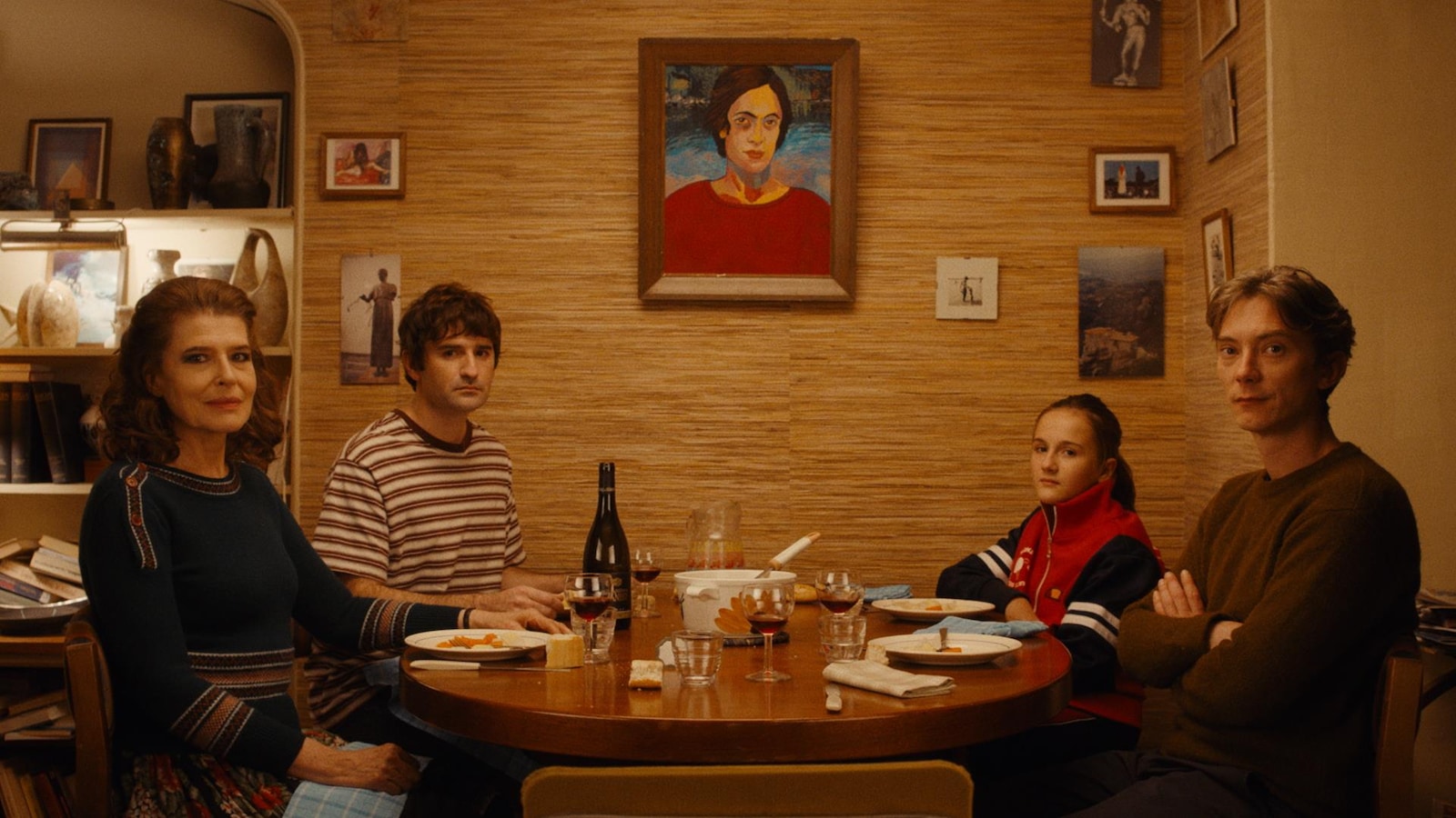 Une femme (Fanny Ardant), deux hommes et une petite fille, assis autour d'une table, regardent la caméra. Une femme (Fanny Ardant), deux hommes et une petite fille, assis autour d'une table, regardent la caméra.