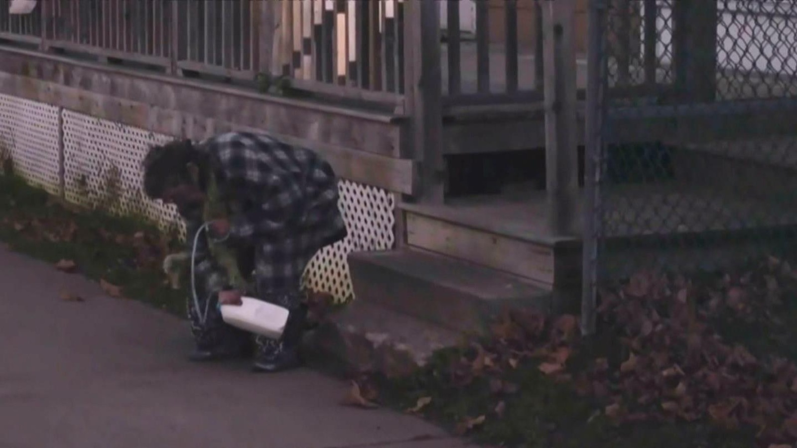 Une personne âgée est penchée devant une maison et tient un pinte de lait en plastique avec une laisse. Une personne âgée est penchée devant une maison et tient un pinte de lait en plastique avec une laisse.