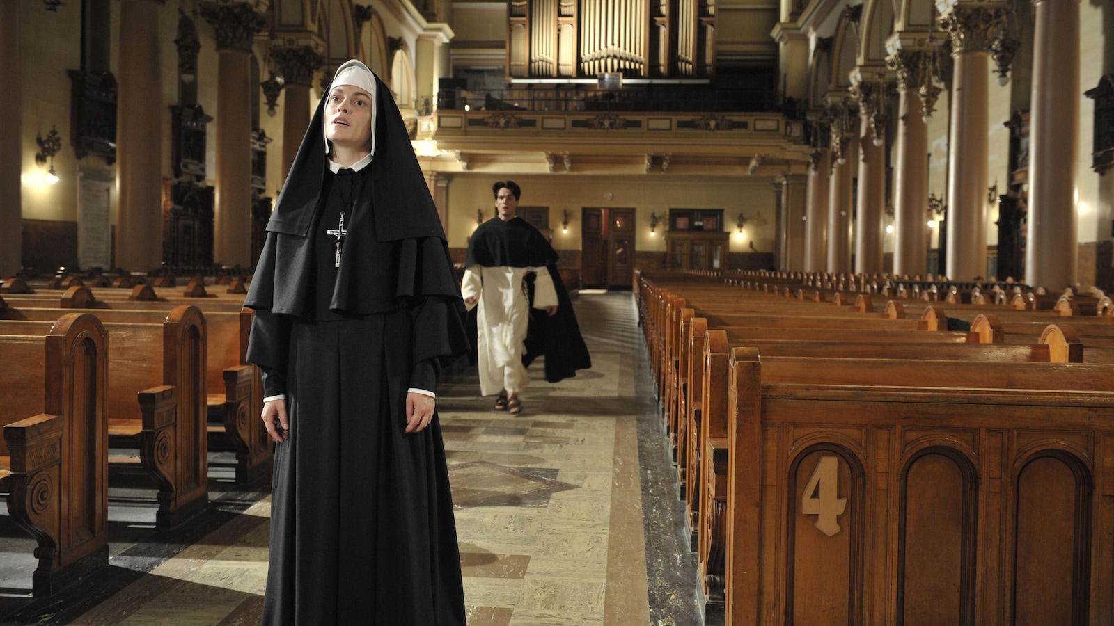 Une soeur en tenue, au milieu d'une église. Un prêtre arrive derrière elle. Une soeur en tenue, au milieu d'une église. Un prêtre arrive derrière elle.