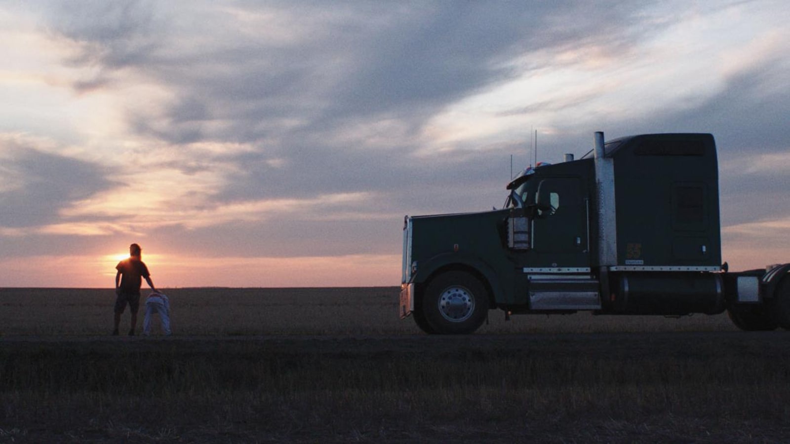 Devant un soleil couchant, et à droite d'un camion immobilisé, un homme et une fillette de dos. Devant un soleil couchant, et à droite d'un camion immobilisé, un homme et une fillette de dos.