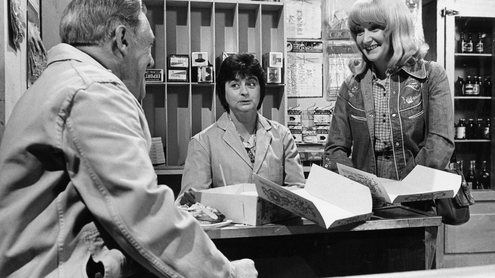 À l'intérieur de son épicerie, Anatole Marsouin (Rolland Bédard) discute avec Inonda Dugas (Reine France) et Doudou Désiré (Louise Deschâtelets). À l'intérieur de son épicerie, Anatole Marsouin (Rolland Bédard) discute avec Inonda Dugas (Reine France) et Doudou Désiré (Louise Deschâtelets).
